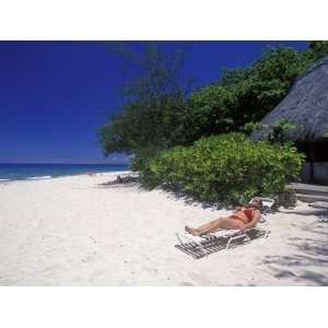 Woman Relaxing on a White Sand Beach in Front of a Bure Hut Stretched 