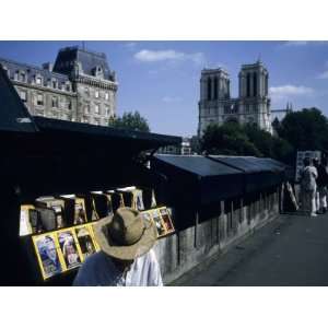  A Man Sells Magazines Along the Seine River with Notre 